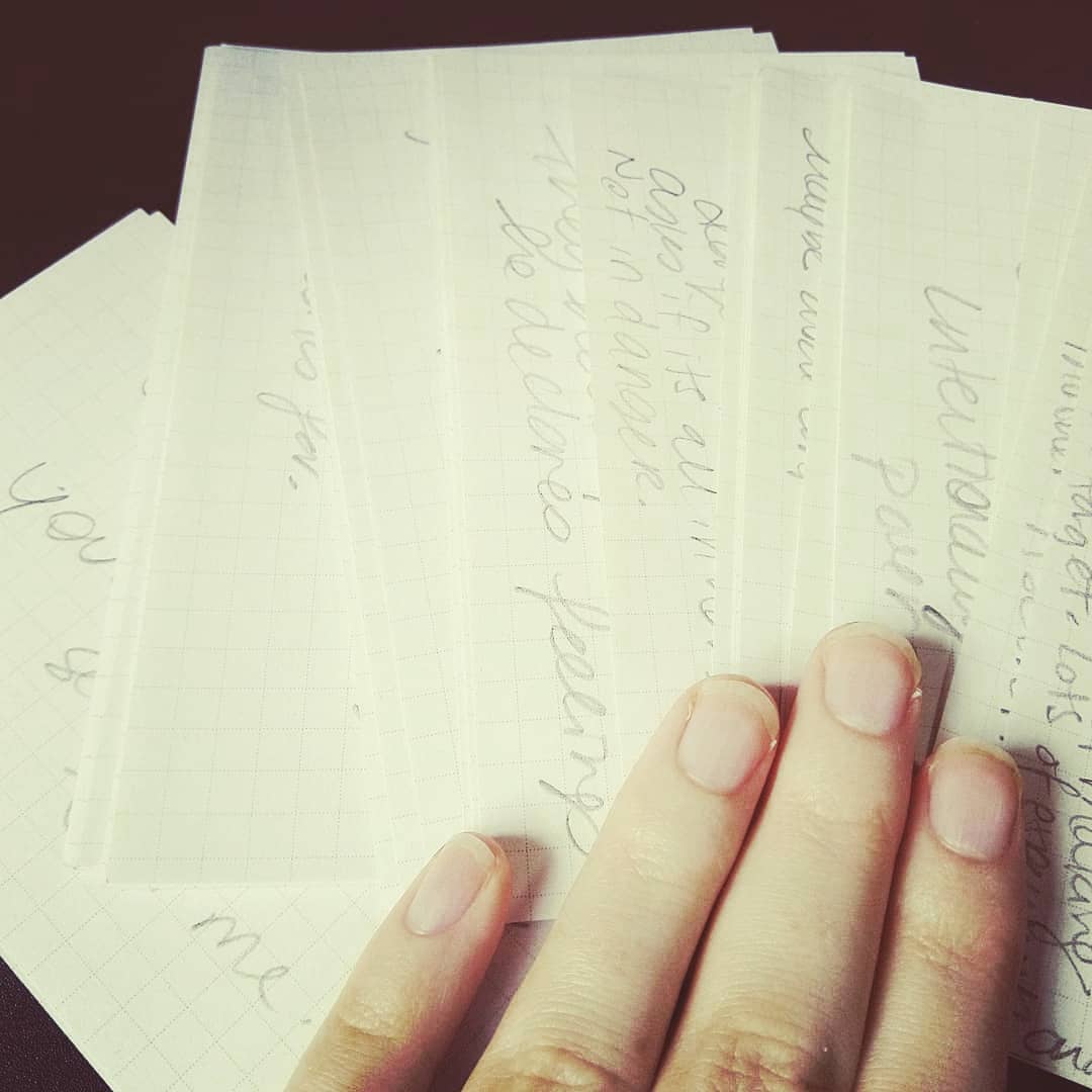 fingers rest on a pile of index cards. The cards are spread in a fan, each showing a peak of handwriting in pencil.